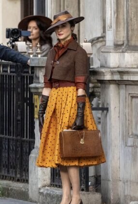 Rachel Weisz de chap&eacute;u, jaqueta marrom e saia amarela de bolinhas em rua de Londres